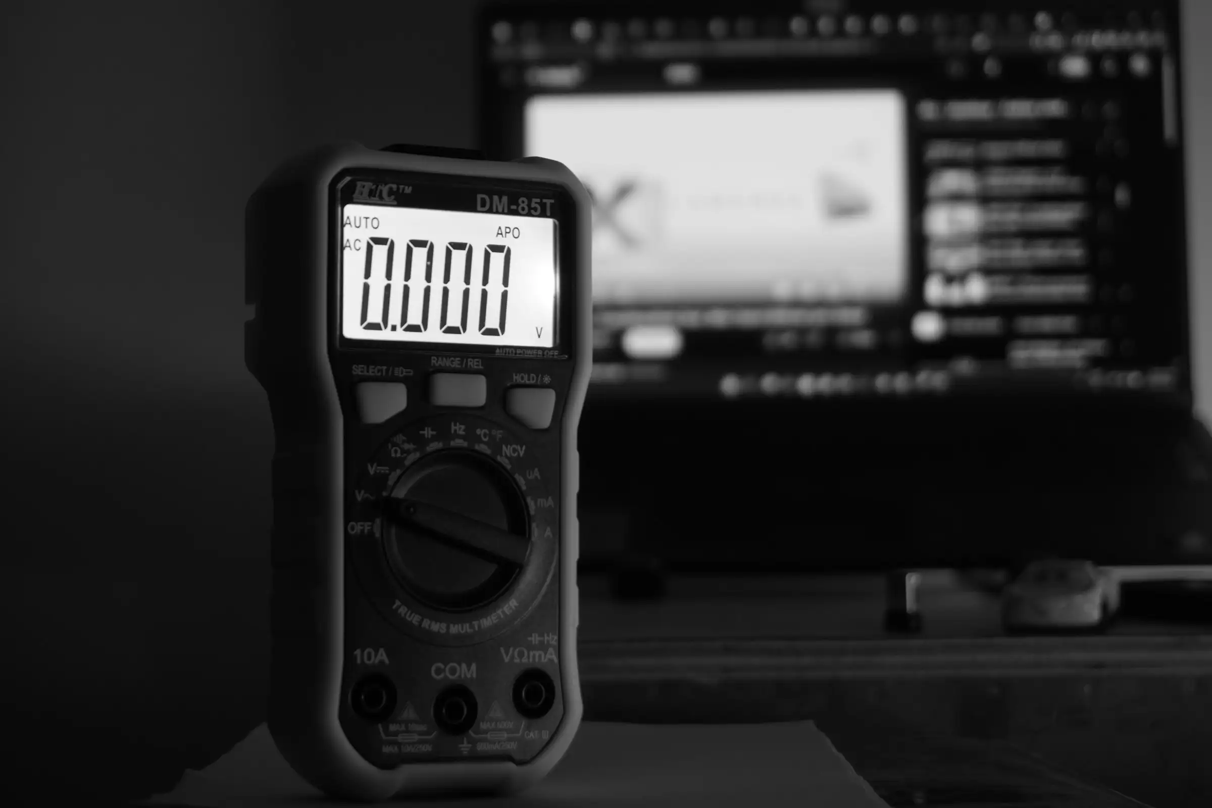 Digital multimeter on a desk in front of a computer screen